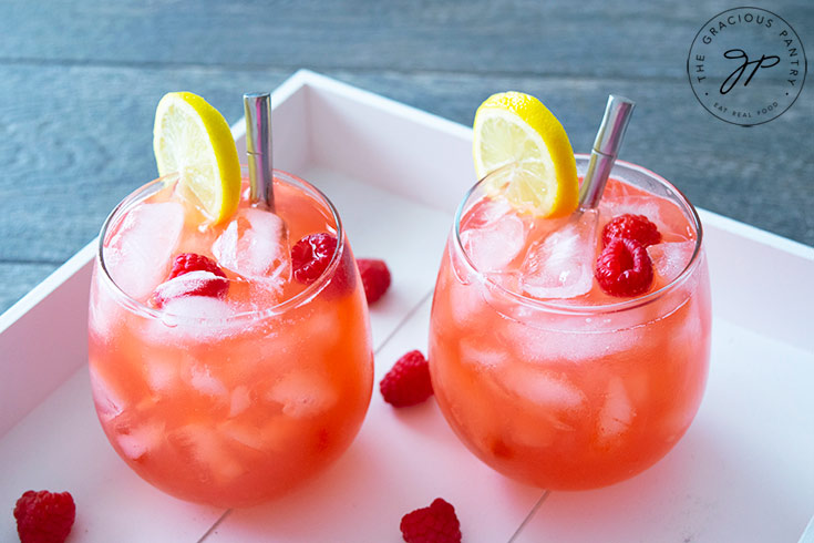 Two glasses filled with raspberry lemonade sit on a white serving tray, ready to serve.