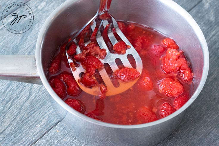 Step one of this raspberry lemonade recipe shows the raspberries getting mashed in a pot.