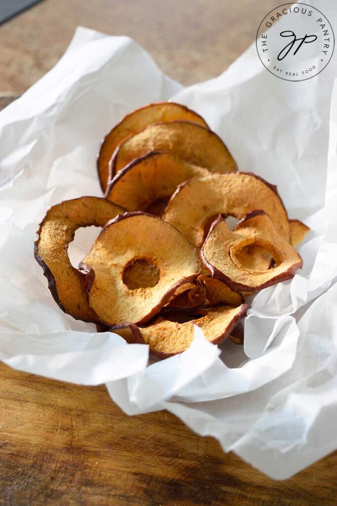 Air Fryer Apple Chips in crinkled parchment sitting on a wooden table.