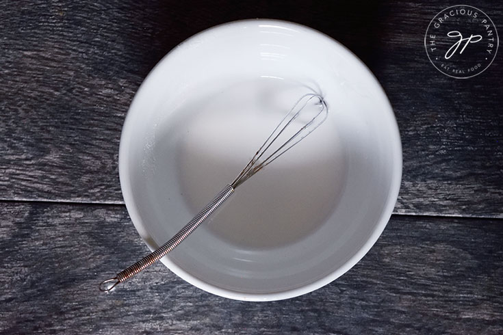 A white bowl sits with a small whisk in a small puddle of slurry.