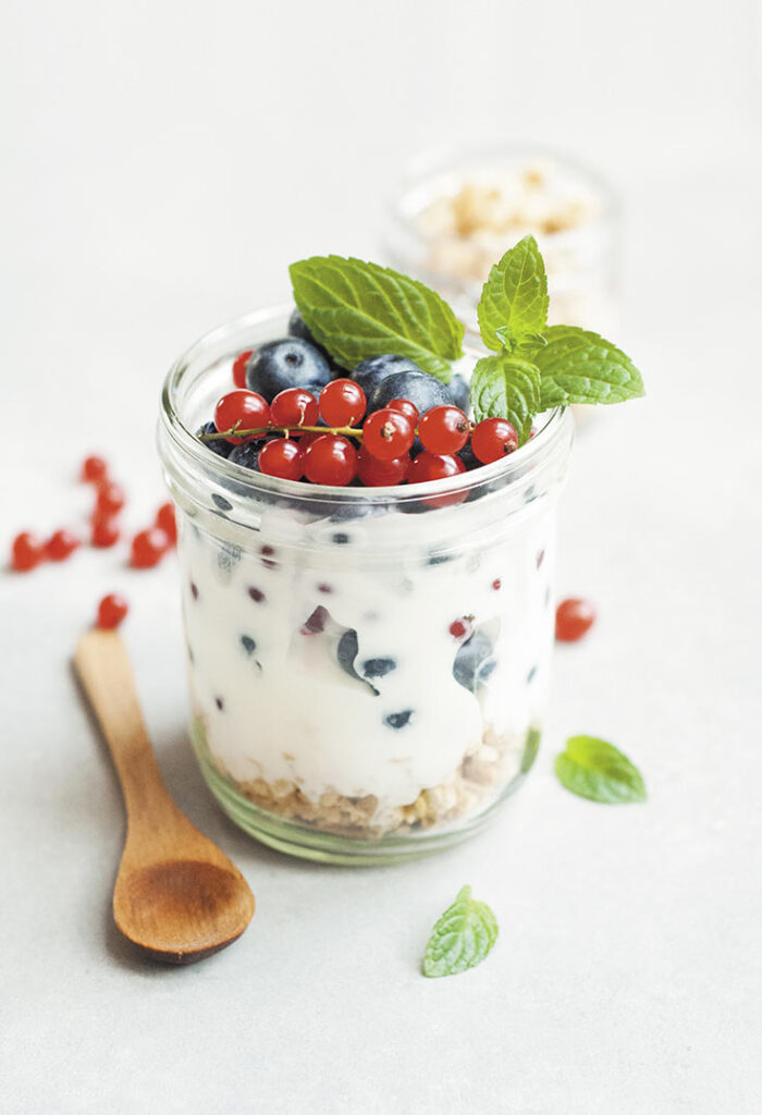 A glass jar filled with granola, yogurt and topped with fresh berries and mint leaves. A great addition to this list of 300 calorie meals.