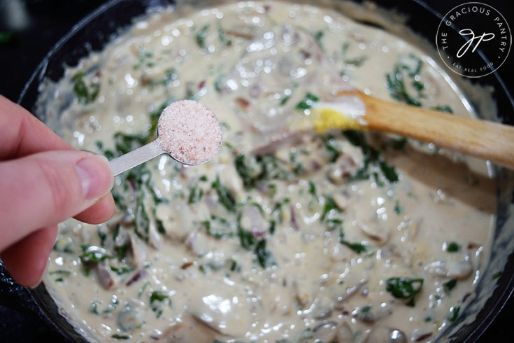 Adding salt to Creamy Kale And Mushroom Pasta sauce in a skillet.