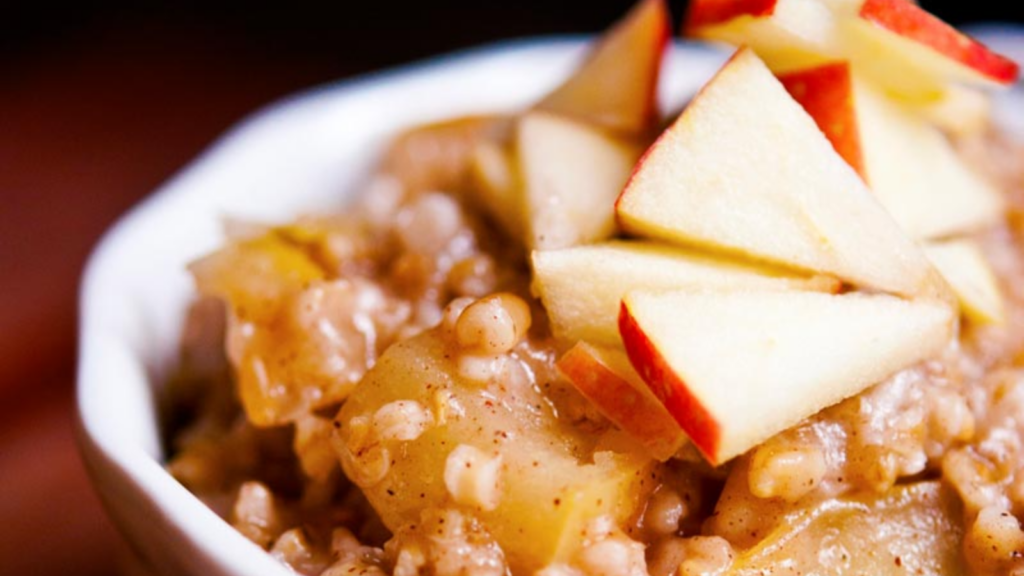 A closeup of a white crock filled with apple pie oatmeal and garnished with fresh apple pieces.