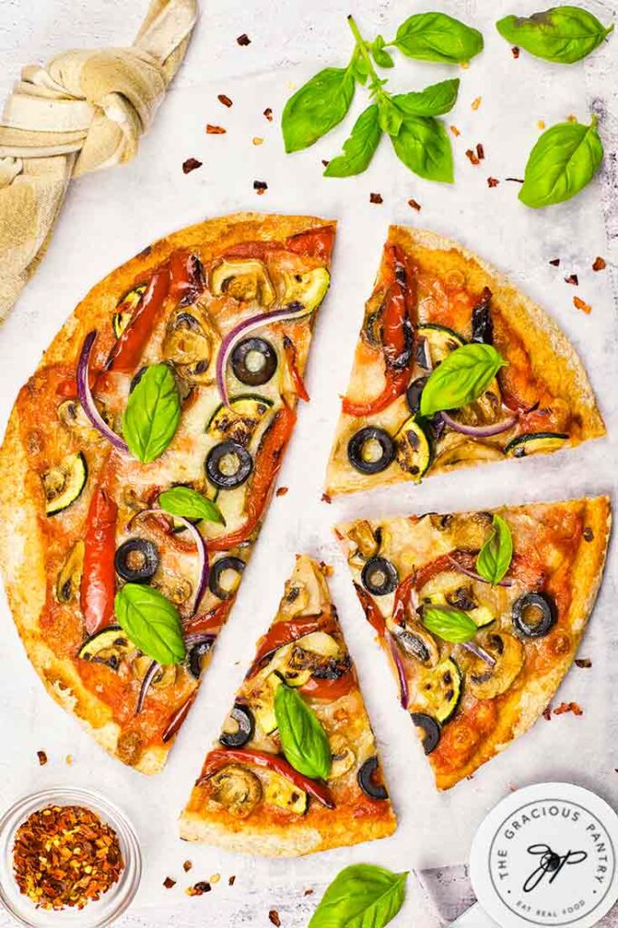 A veggie pizza with half cut away and sliced.