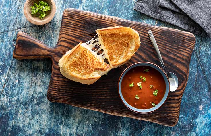 An overhead view of a bowl of tomato soup sitting next to a cut grilled cheese sandwich.