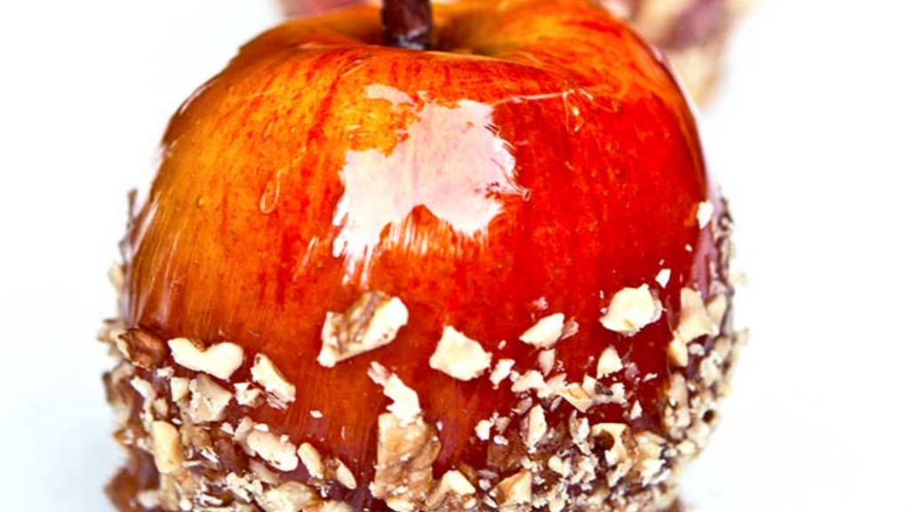 A closeup of a single candied apple with nuts stuck to the side.