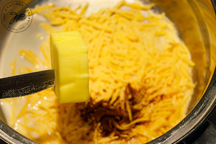Adding butter to milk cheese and spices in a pot.