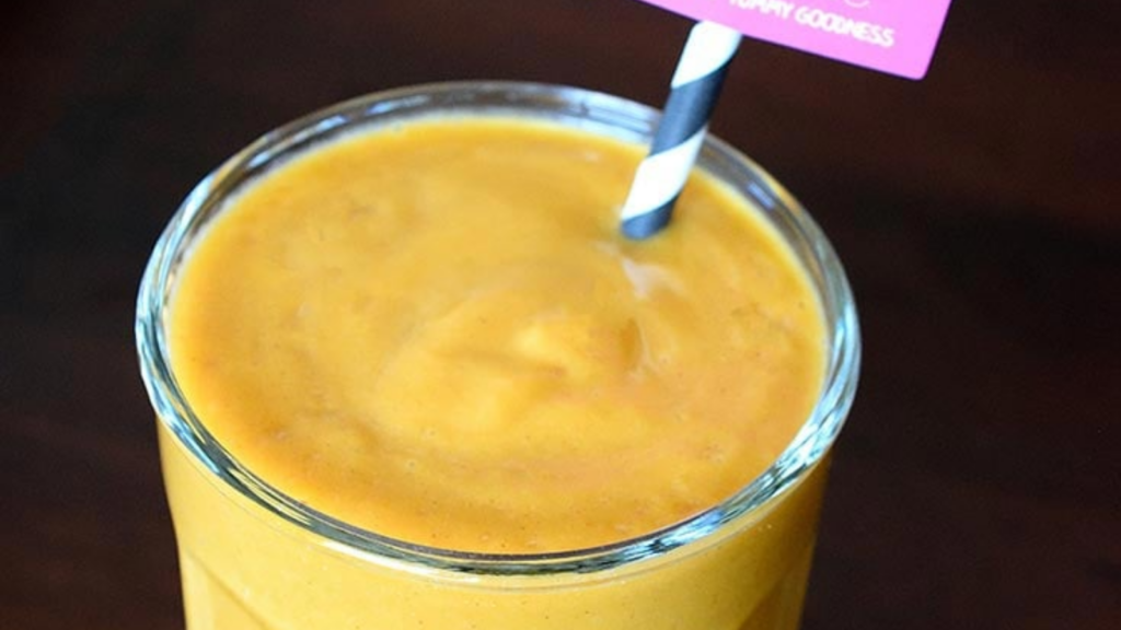 A sweet potato smoothie in a clear glass with a straw in it.
