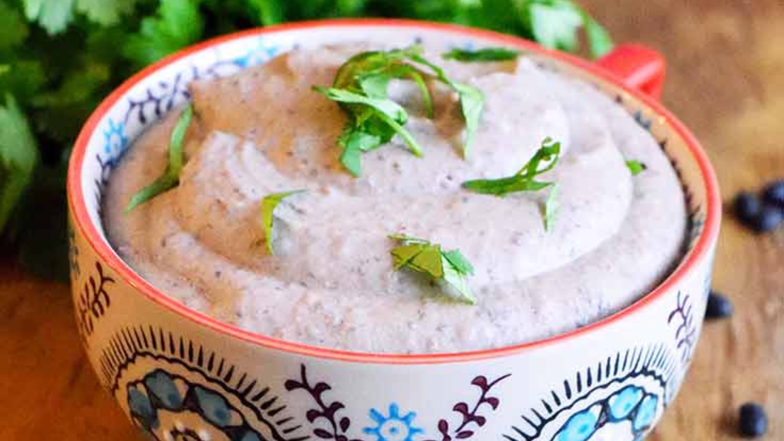 A decorative bowl filled with black bean hummus and garnished with fresh, chopped herbs.
