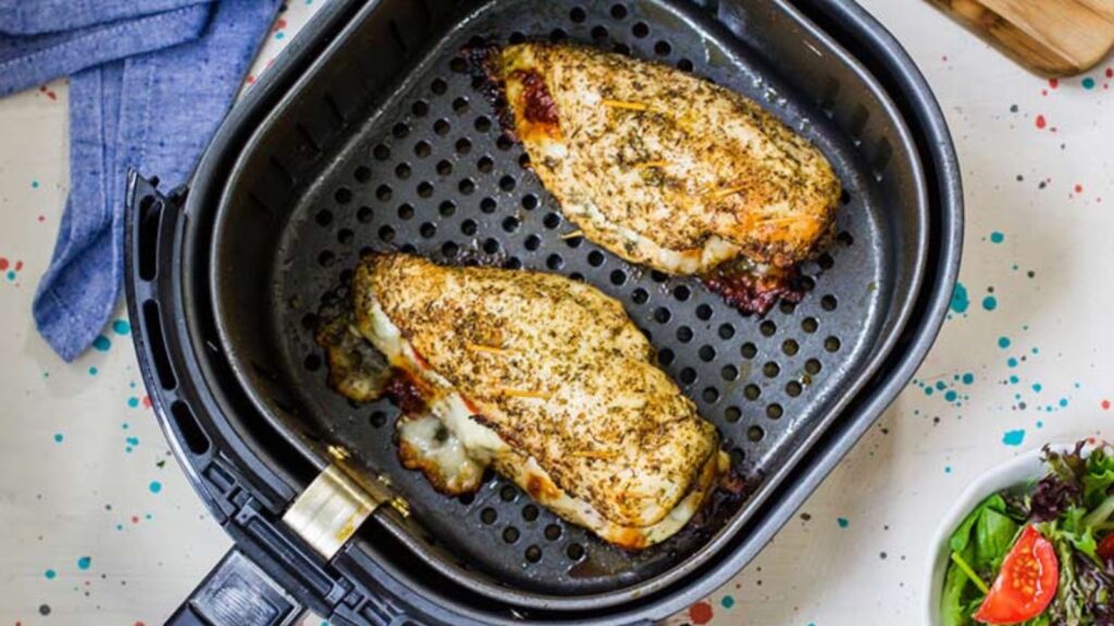 Two chicken breasts in an air fryer basket.