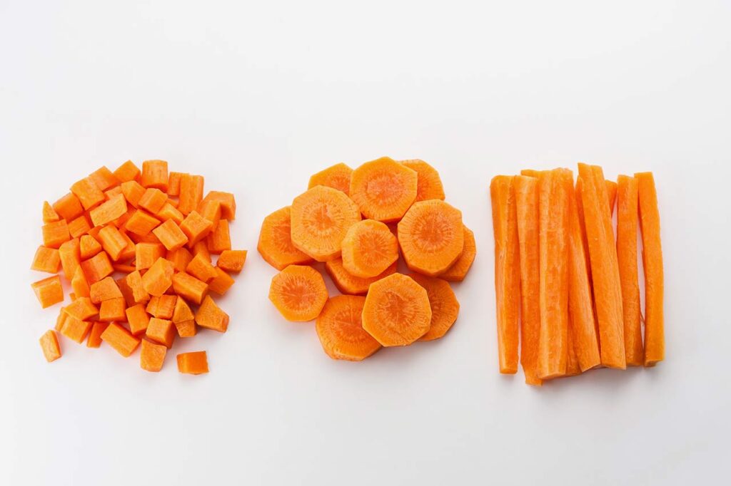 Carrots cut into uniform sizes, separated into three piles. Diced, sliced, and sticks.