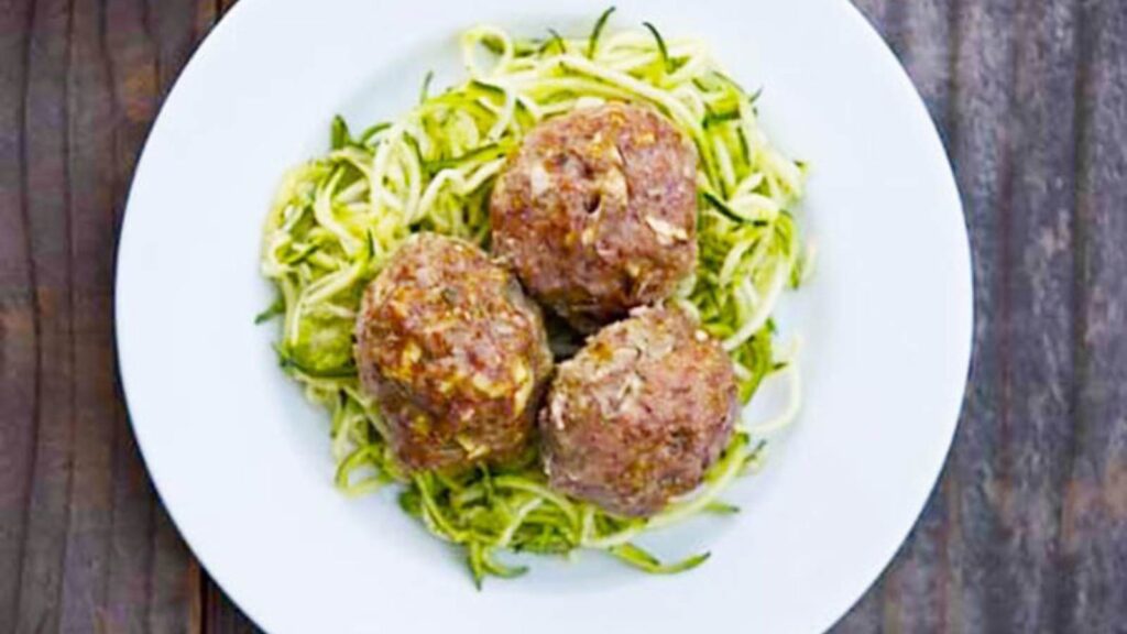 Three large meatballs on a bed of zucchini noodles on a white plate.