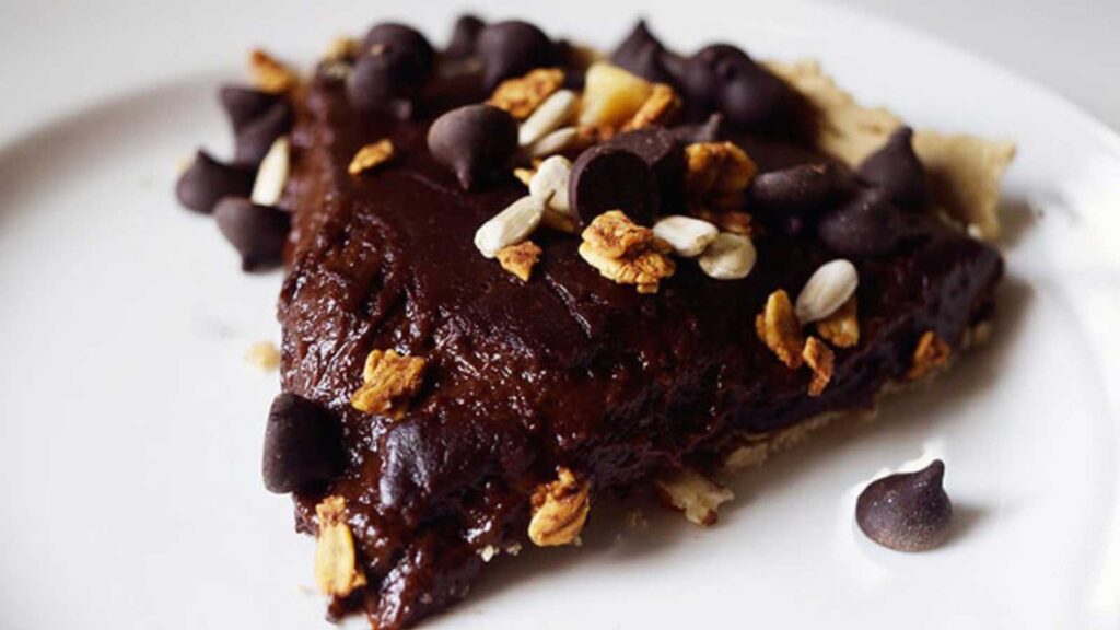 A single slice of Chocolate Pie sitting on a white plate, garnished with chopped nuts and chocolate chips.