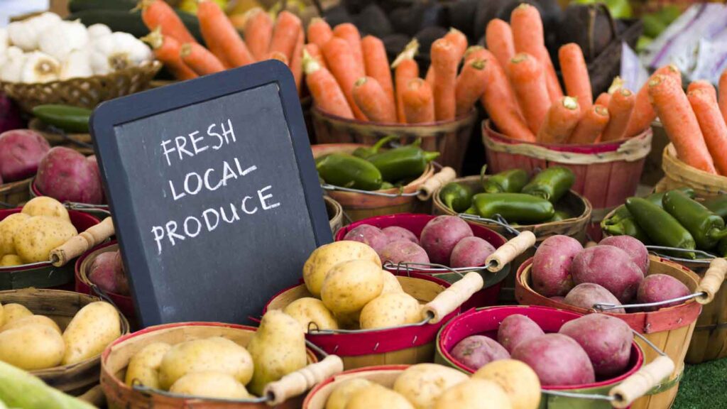 A sign says, "Fresh, local produce", amidst baskets of fresh, market produce.