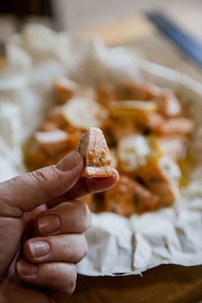 A hand holds up an air fryer salmon bite from a basket full of them.