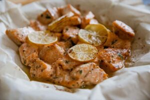 A parchment-lined basket filled with air fryer salmon bites topped with lemon slices.