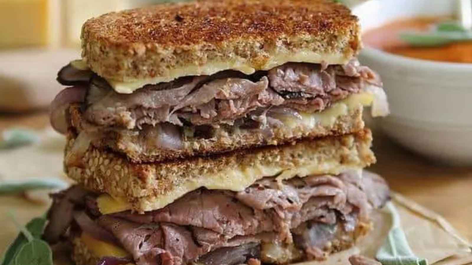 A closeup of a halved and stacked roast beef and smoked gouda grilled cheese sandwich.