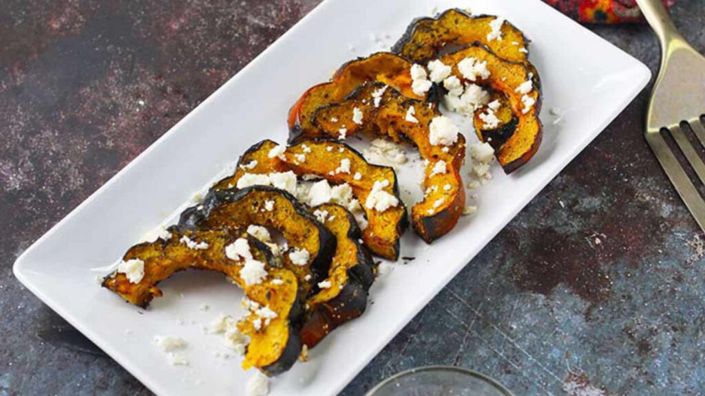 Roasted Acorn Squash With Feta recipe on a white platter, garnished with feat cheese crumbles.