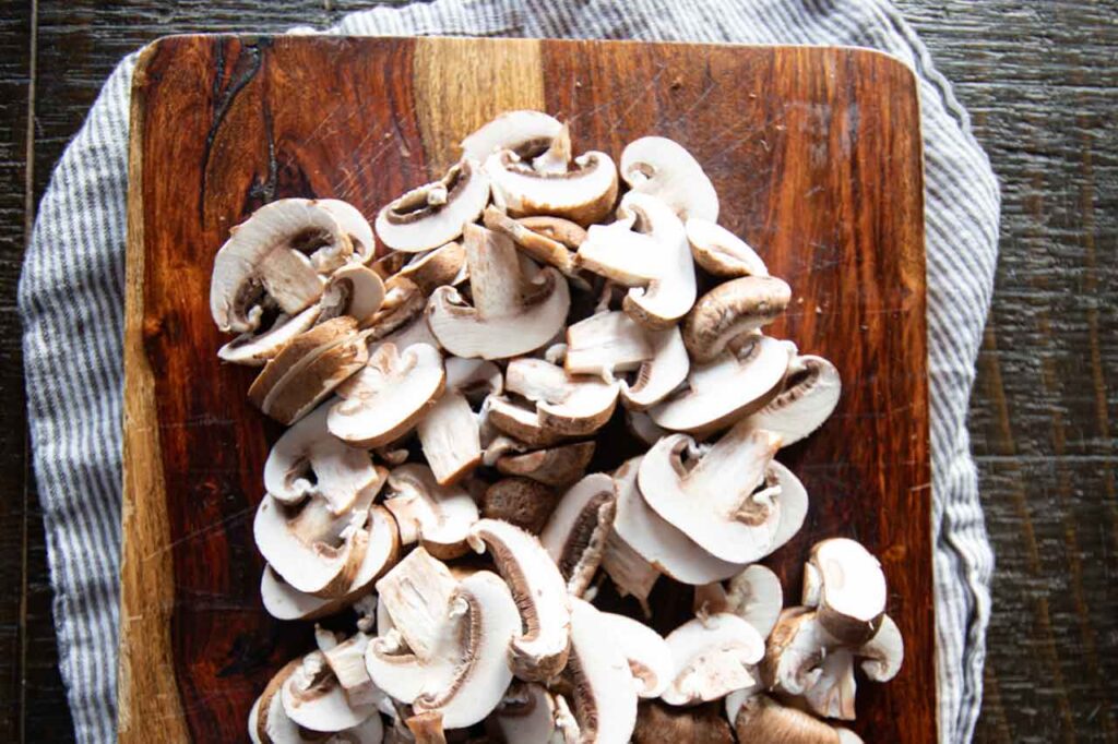 Raw sliced mushrooms on a cutting board.