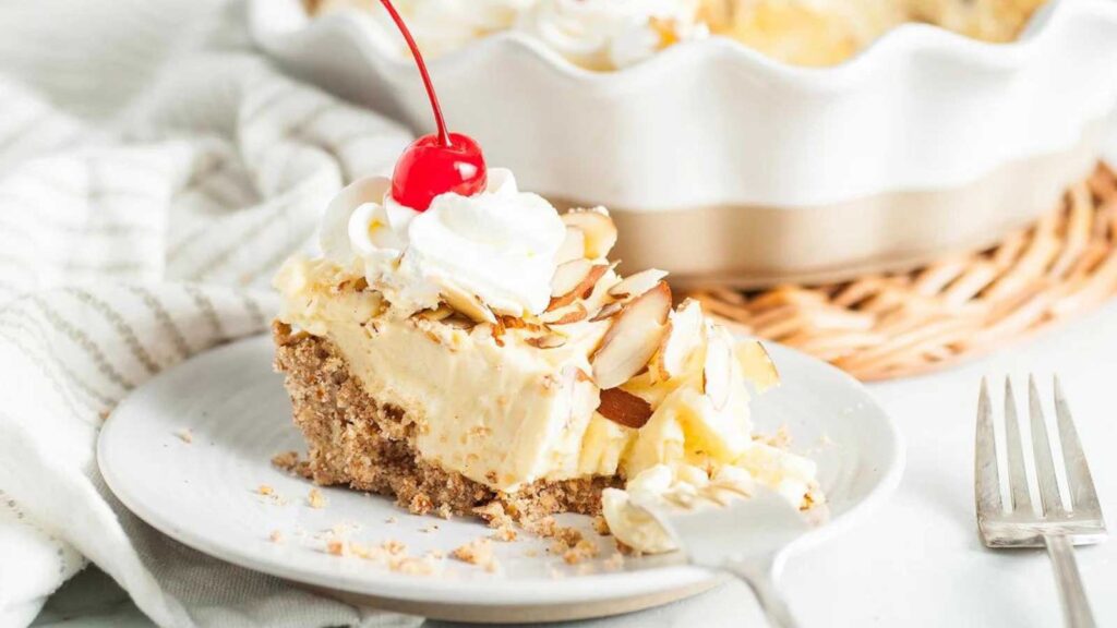 A slice of partially eaten amaretto cream pie with an almond crust on a white plate with a fork.
