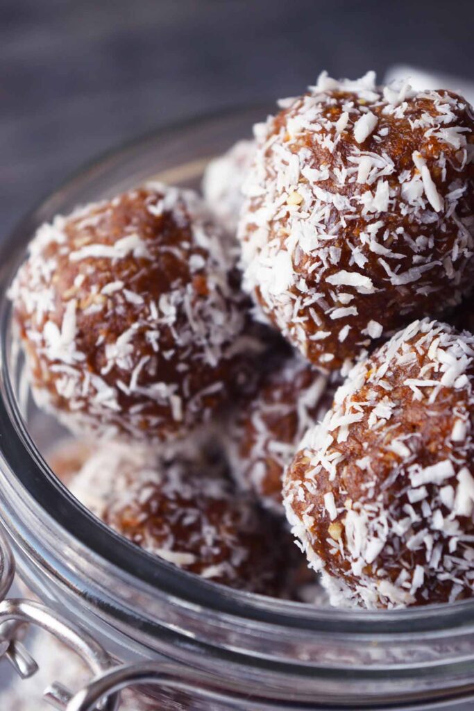 An up-close side view of an open glass jar full of Date And Oat Energy Balls.