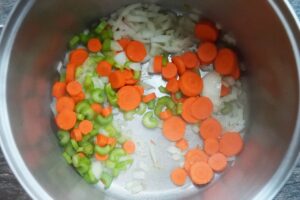 Sliced carrots and celery added to chopped onions and oil in a pot.