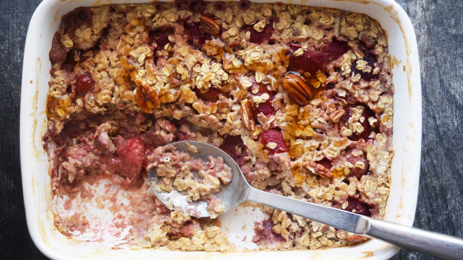 An overhead view of a partially eaten Baked Oatmeal With Strawberries in a casserole dish.