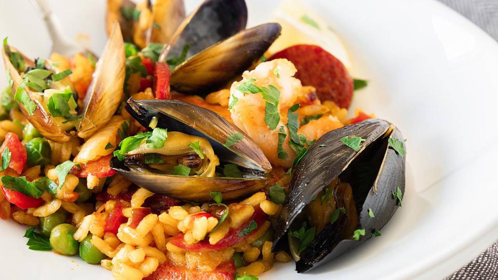 A closeup of a white bowl filled with Seafood Paella with Mussels, Shrimp and Chorizo.