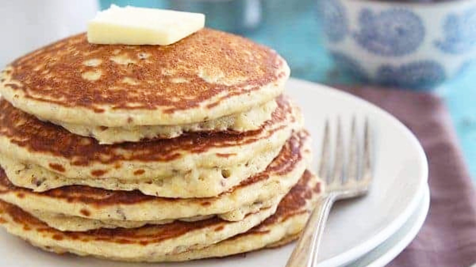 A stack of pancakes on a plate with a pt of butter on top.