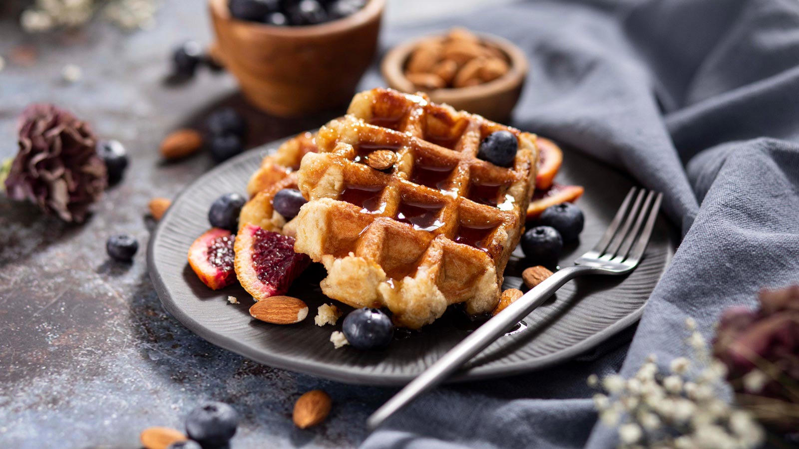 A plate holds homemade almond flour waffles drizzled with syrup and fresh blueberries.