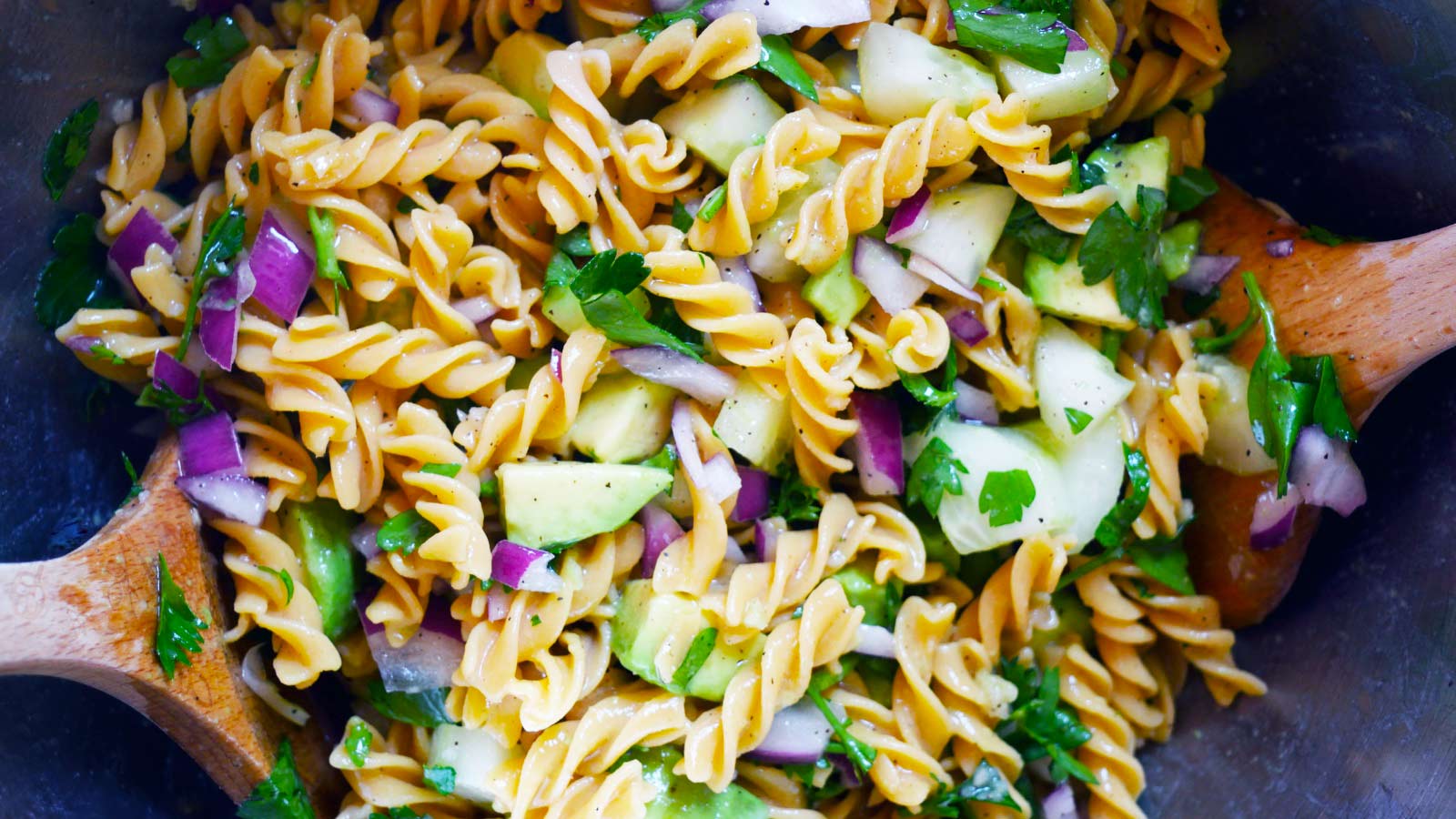 A close up of a large mixing bowl filled with Avocado Pasta Salad.
