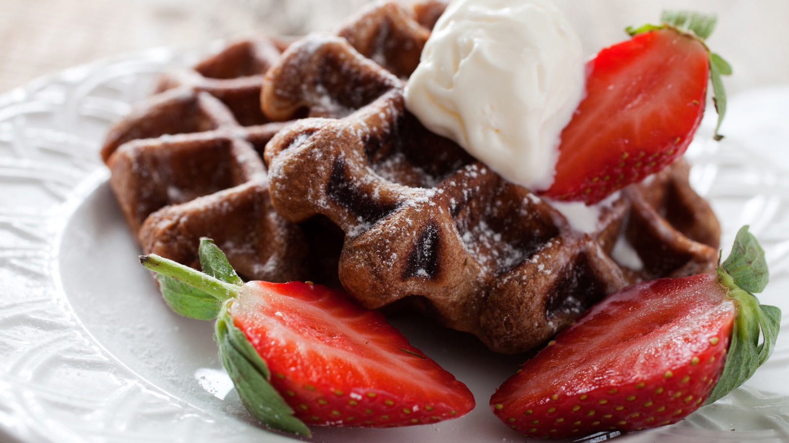Two brownie waffles on a white plate with fresh cut strawberries and a dollop of whipped cream.