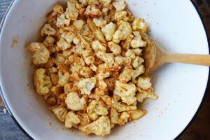 Seasoned, raw cauliflower mixed with spices in a mixing bowl.