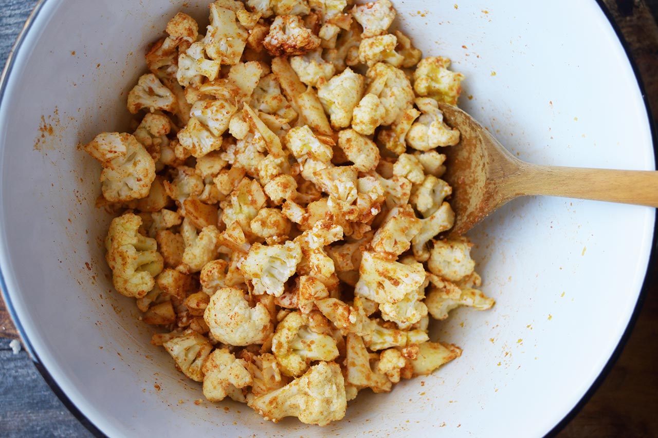 Seasoned, raw cauliflower mixed with spices in a mixing bowl.