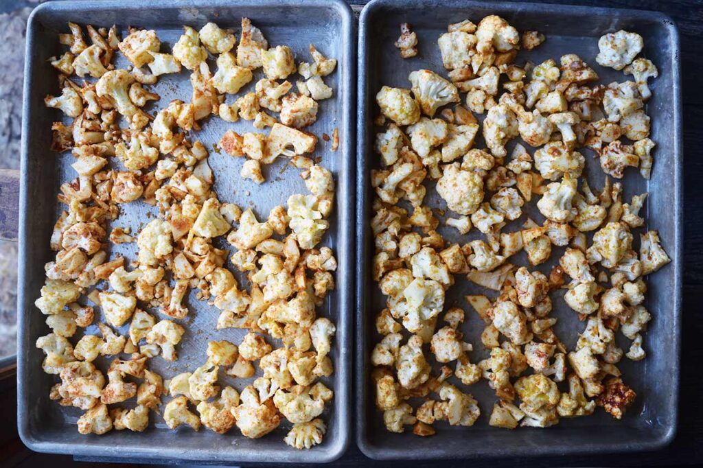 Raw bits of seasoned cauliflower spread out over two sheet pans or roasting.