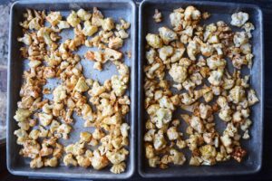 Raw bits of seasoned cauliflower spread out over two sheet pans or roasting.