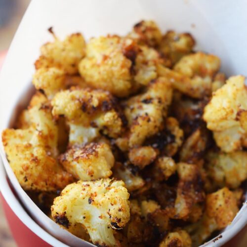 A red, parchment-lined mug filled with cauliflower popcorn.