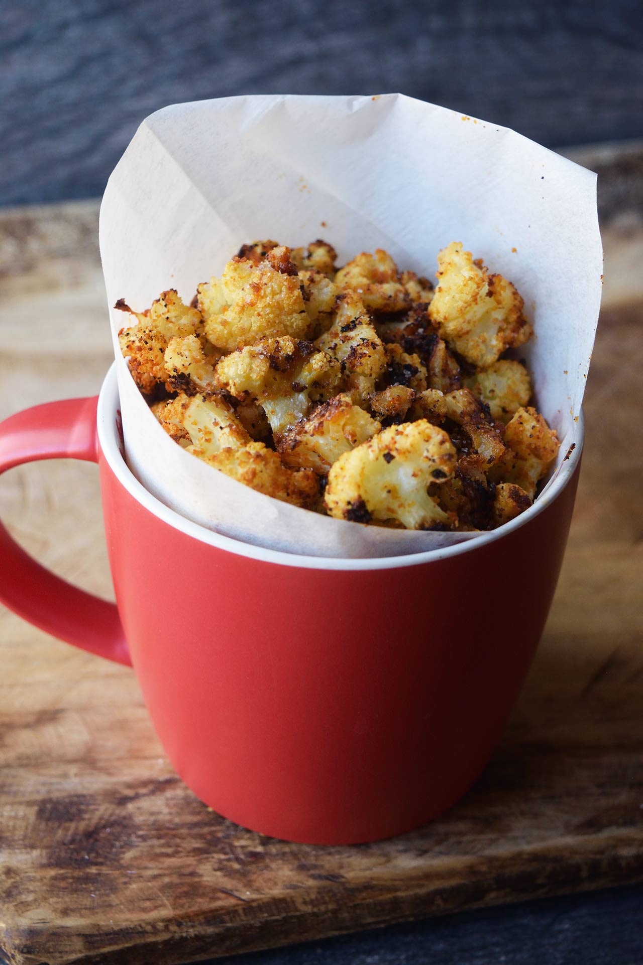 A side view of a red mug filled with cauliflower popcorn.