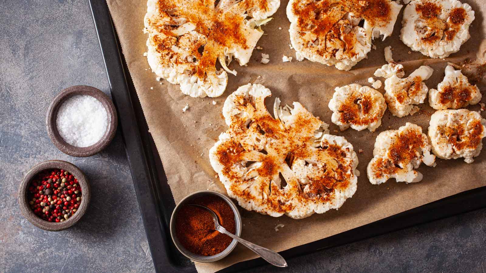 Cauliflower steaks with spice on baking tray.
