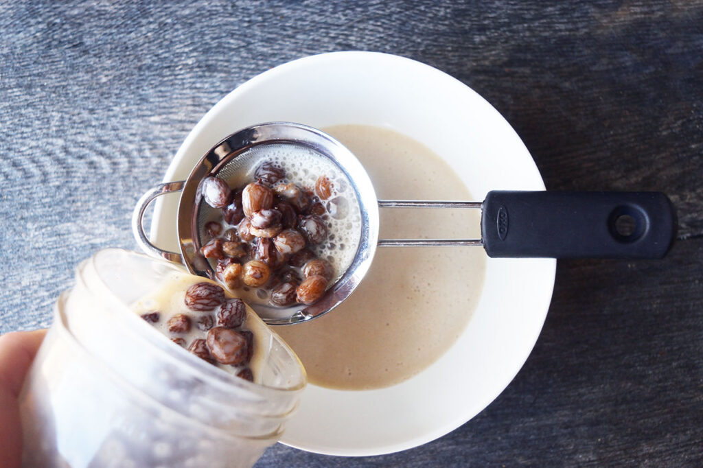 Pouring raisins and condensed milk through a strainer into a bowl.