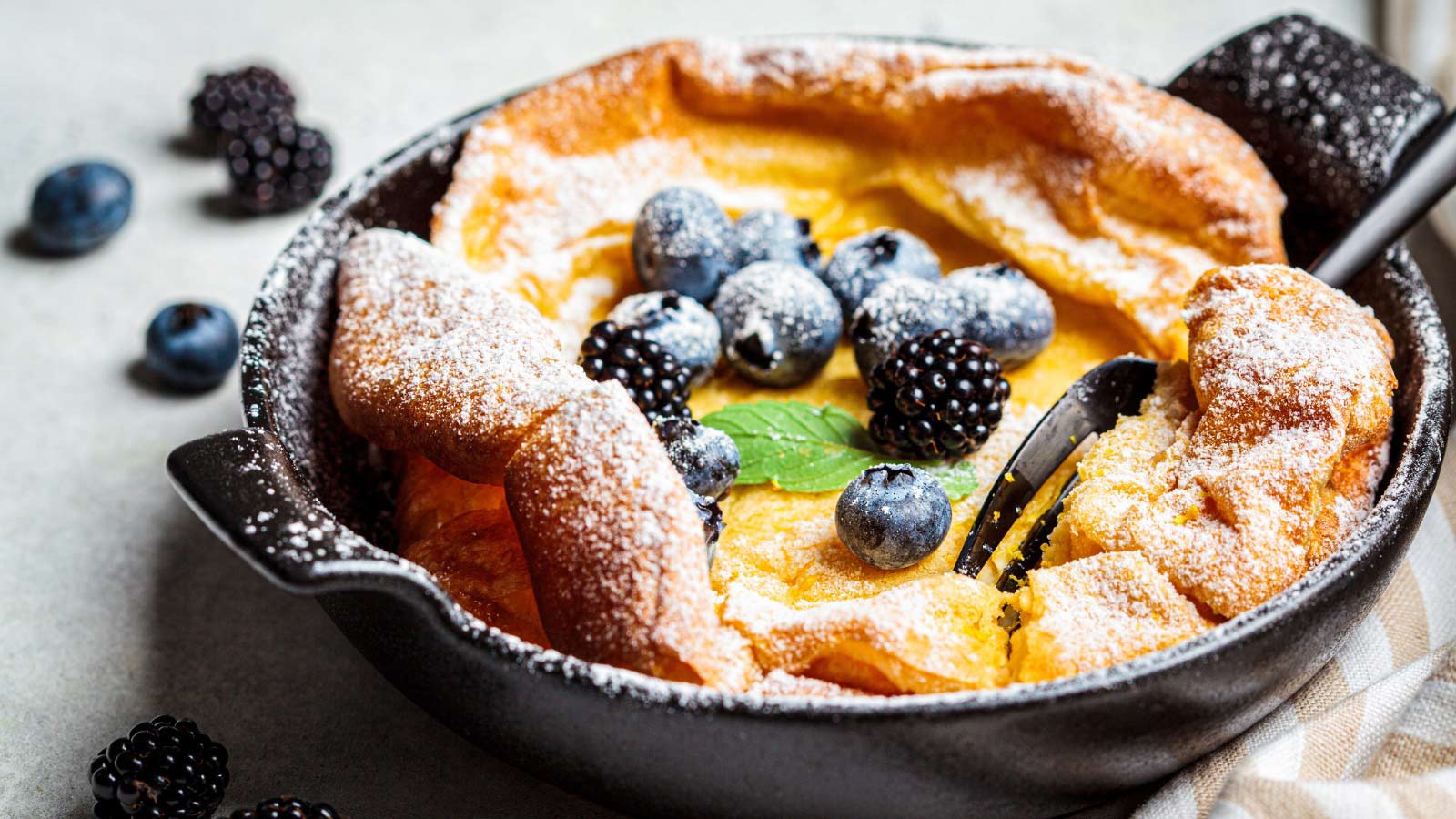 Dutch baby pancake with berries and icing sugar in a pan.
