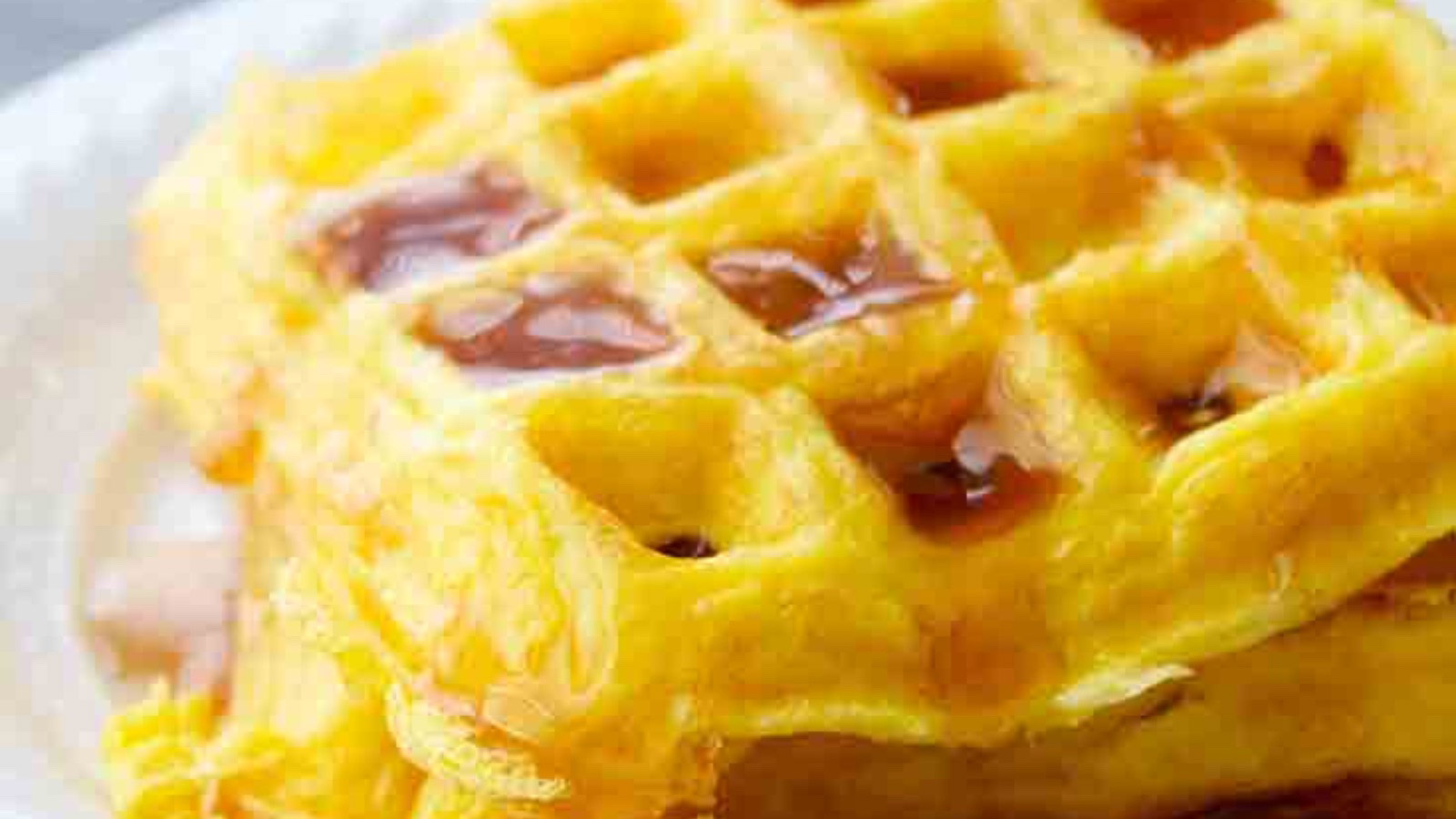A closeup of egg waffles with maple syrup drizzled over the top.