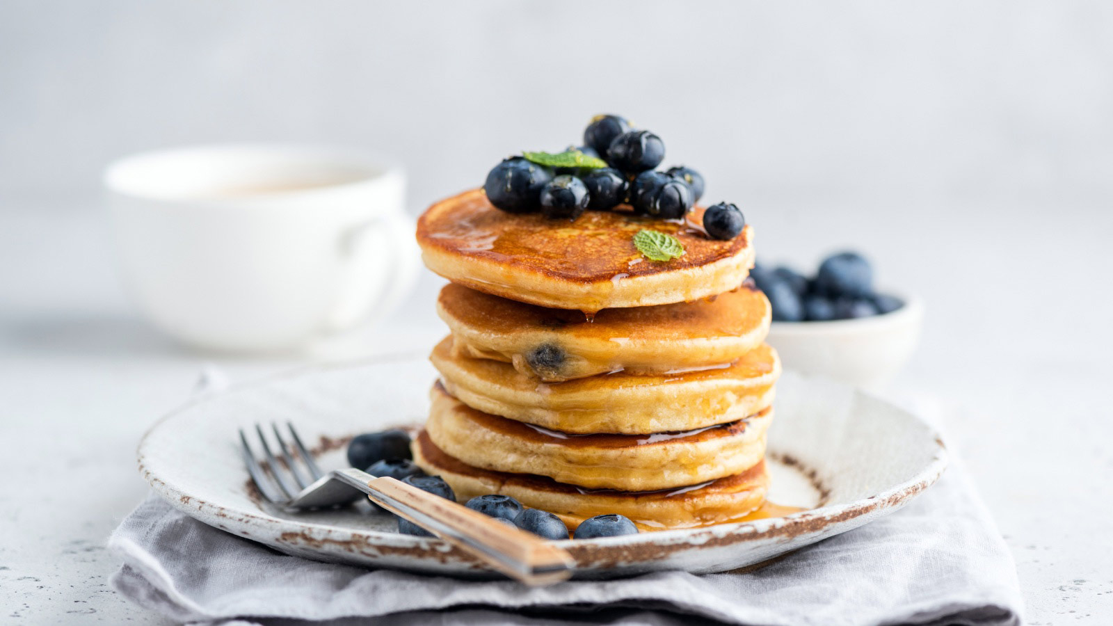 Tasty pancakes with blueberries and honey on a plate. Grey background