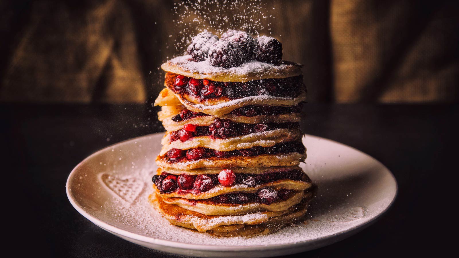 A stack of Pancakes with berries and sugar on a plate.