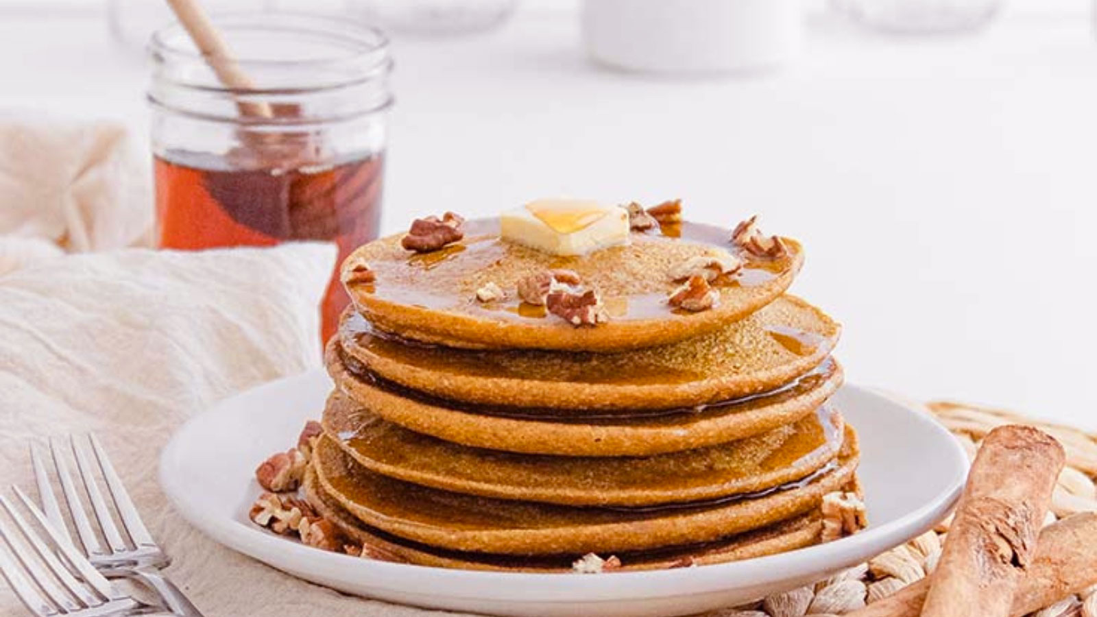 A stack of Pumpkin Oatmeal Pancakes on a white plate, topped with butter, syrup and pecans.