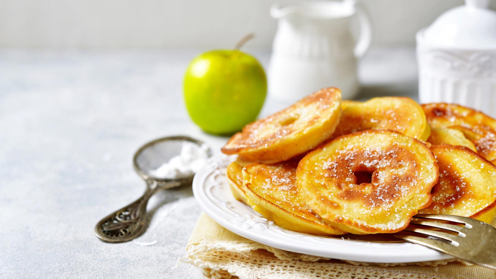 Apple pancakes for a breakfast on white plate over light slate, stone or concrete background.