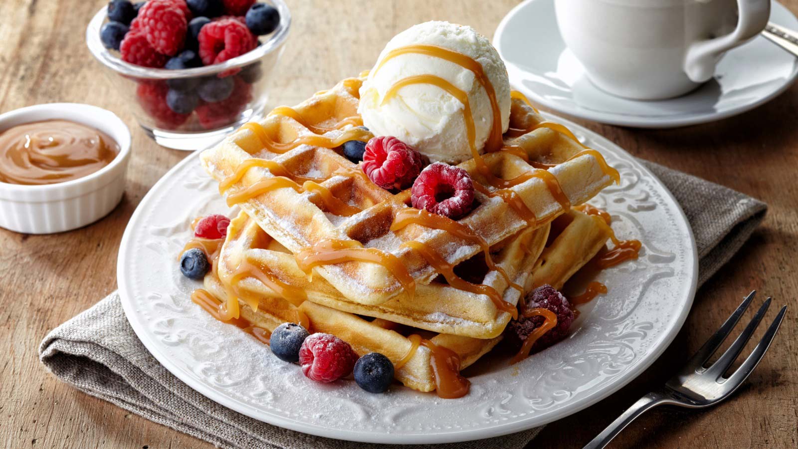 Plate of belgian waffles with ice cream, caramel sauce and fresh berries.