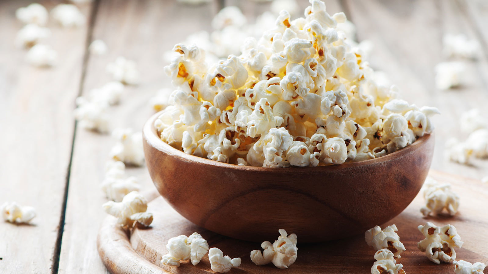Popcorn on the wooden table, in a wooden bowl.