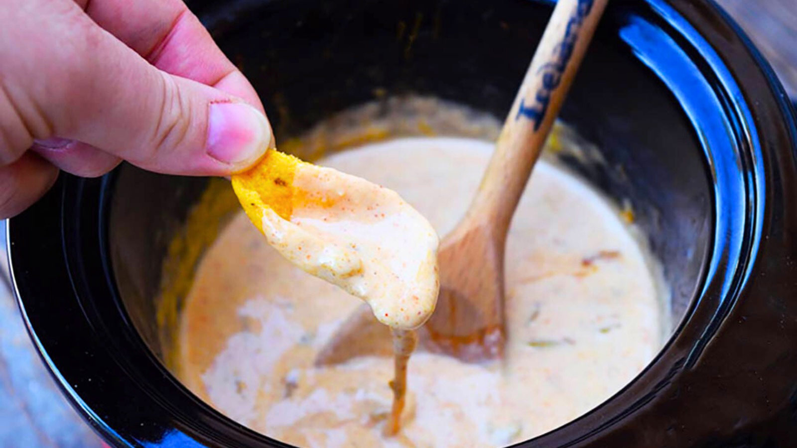 A hand dips a corn chip into homemade queso.