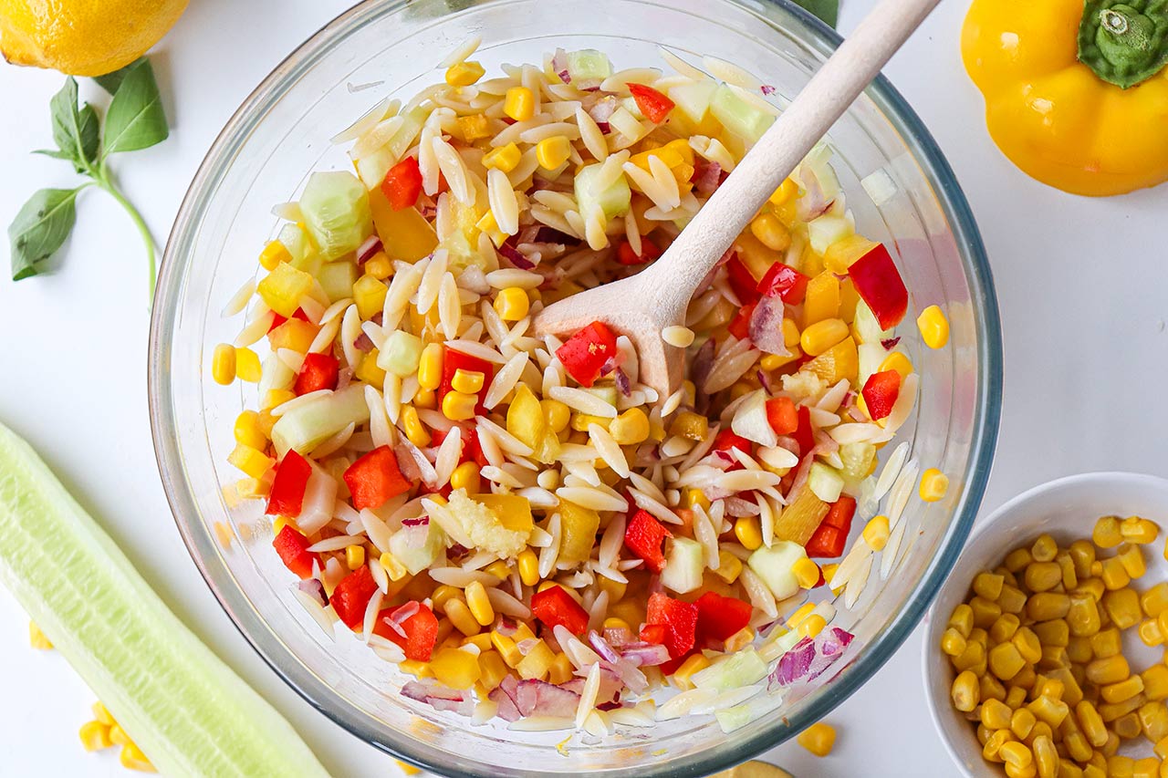 The orzo salad ingredients stirred together in a glass mixing bowl.